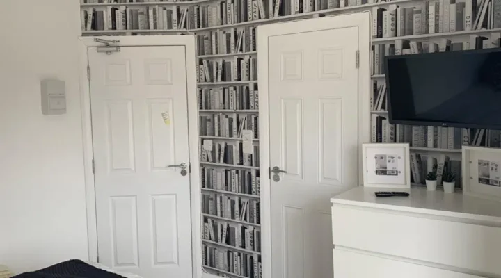 Room with book-patterned wallpaper, TV, and dresser.