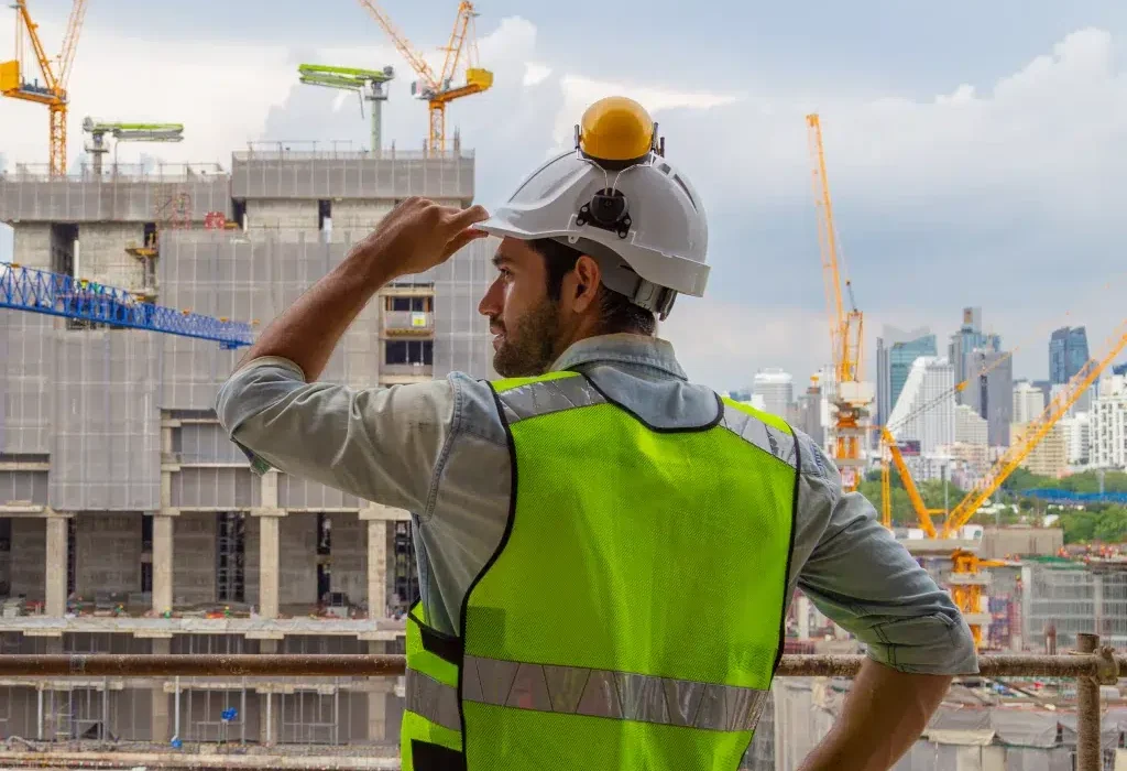 Construction worker surveys urban building site with cranes.
