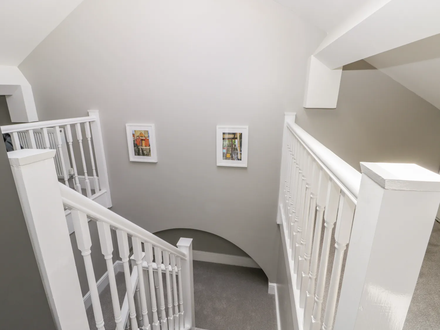 Bright stairwell with white banisters, two paintings.