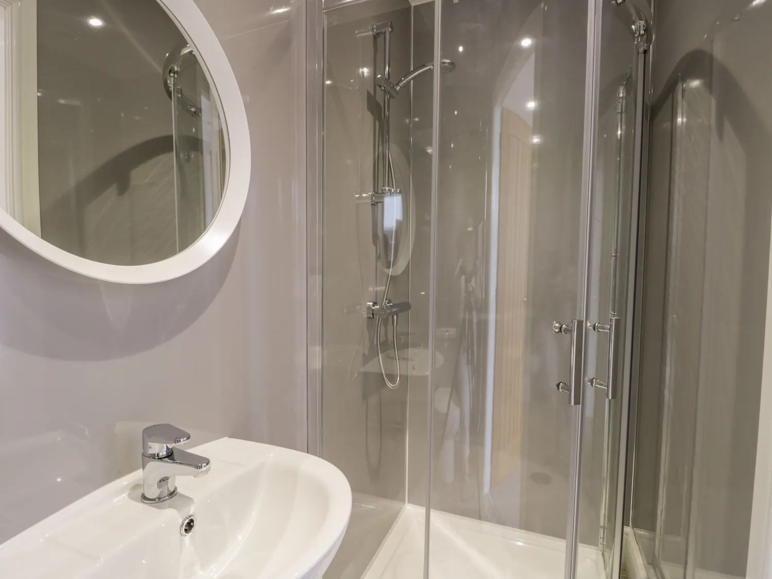 Modern bathroom with glass shower and round mirror.