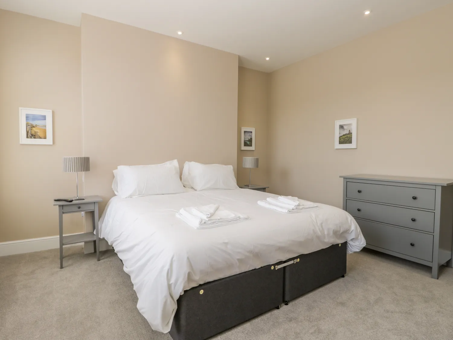 Modern beige bedroom with double bed and dresser.