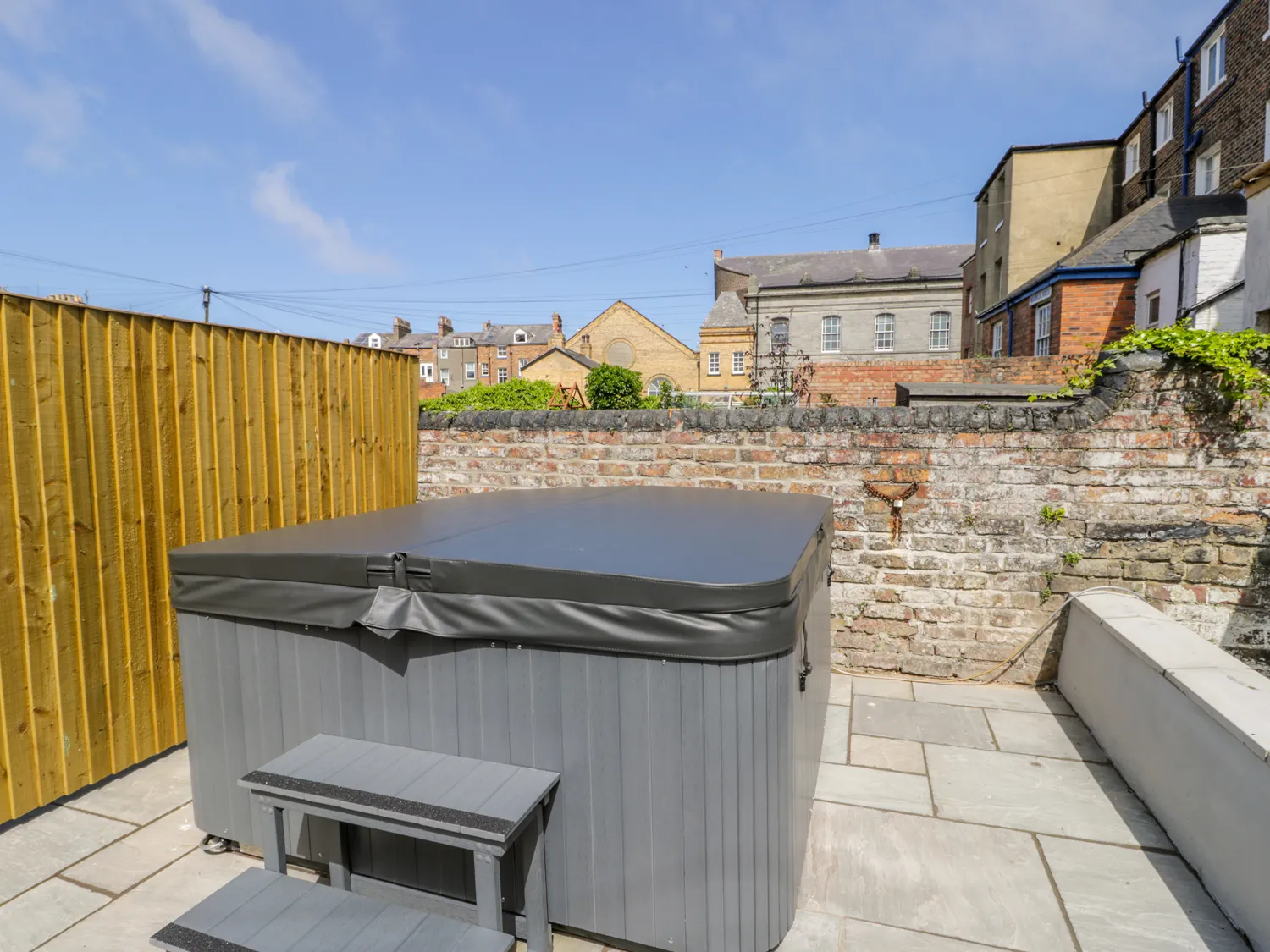 Backyard hot tub with surrounding fence and buildings.